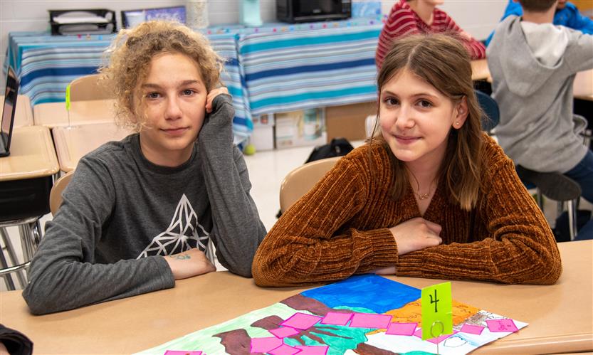 Two girls smile while sitting at school desks